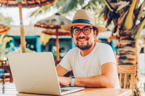 "Joyful freelancer working on laptop in tropical cafe, palm trees in background.