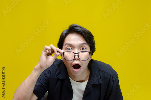 funny expression young asian man shocked happily opening mouth and lowering glasses. asian man with glasses feels shock with wow surprised expression.