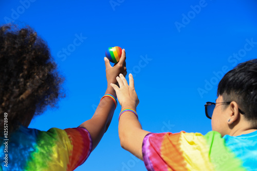 LGBT couple holding rainbow balls and heart-shaped hands together on a relaxing day at the beach.Hands make a heart shape in gay pride.
