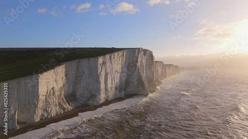 Majestic white cliffs overlook the ocean, with golden light of sunset. Waves crash dramatically below, creating a serene and picturesque landscape that captivates nature enthusiasts. Seven Sisters 