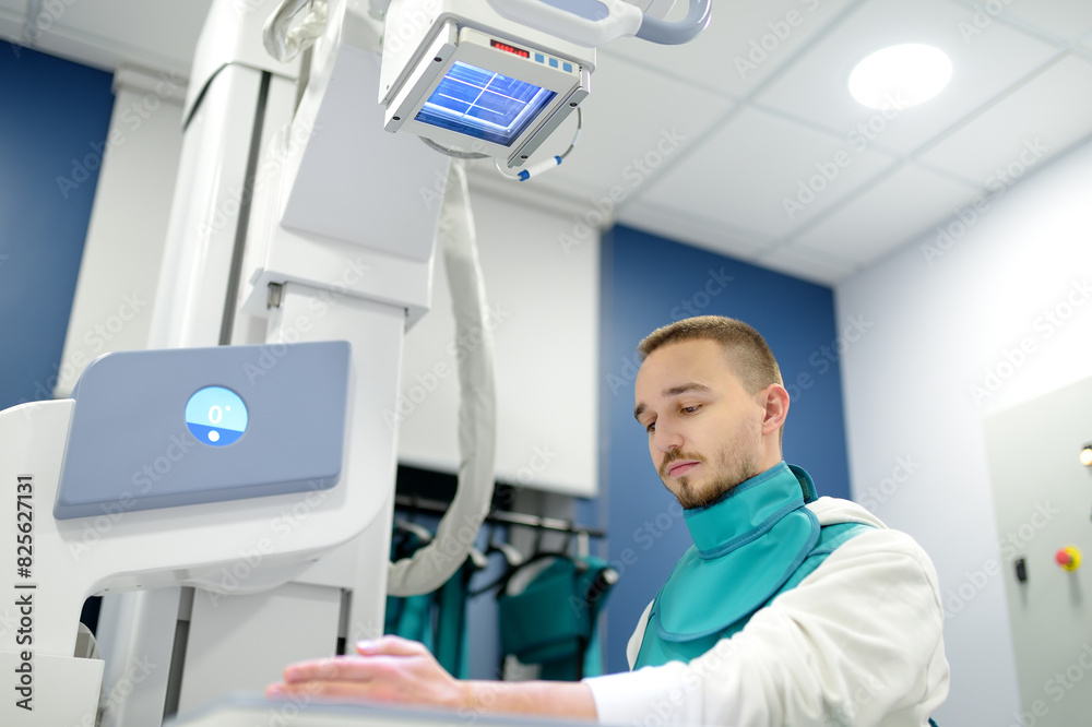 Obraz premium Young man having x-ray shot of broken hand in x-ray room in modern clinic. Patient wearing in protect lead apron