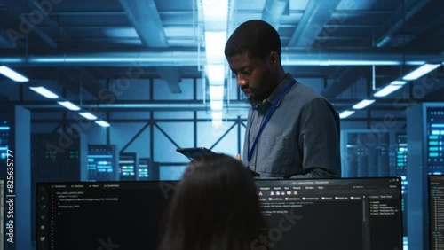 Manager uses tablet, supervising team programming servers providing computing resources for different workloads. Inspector using device to oversee engineers in data center mending supercomputers photo