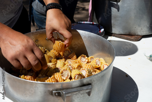 Foto Detalle manos sacando trozos de choclo de una olla popular, gigante
