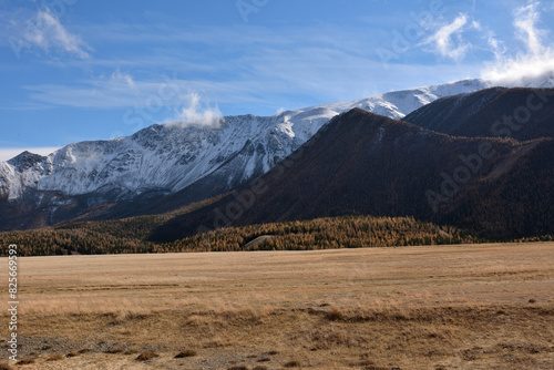 High mountain ranges covered with autumn snow under a cloudy sky on the edge of the endless steppe.