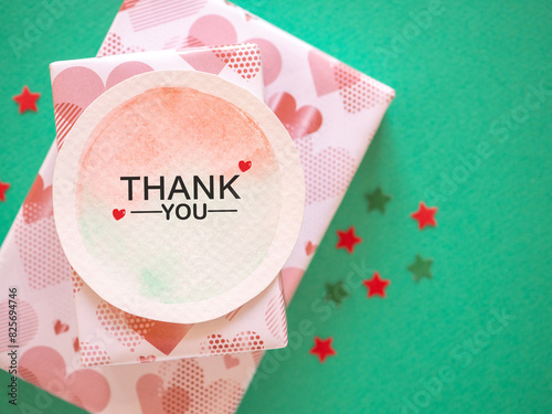 Top view, The word "thank you" message on watercolor paper with gift box and star shape over green paper background. .