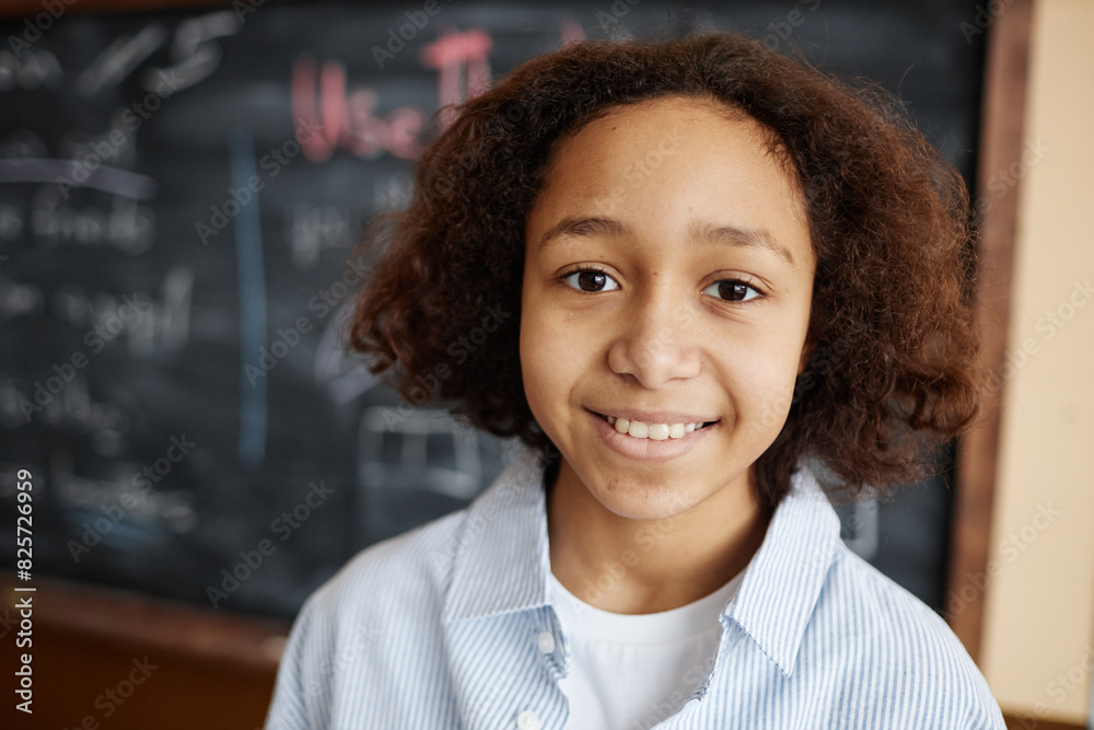 Closeup portrait of cheerful African American boy standing against blackboard in classroom smiling at camera, copy space Closeup portrait of cheerful African American boy standing against blackboard in classroom smiling at camera, copy space