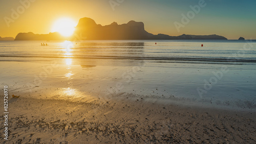 A calm romantic sunset on a tropical island. The setting sun is shining from behind the mountains. A sunny path on the water. Reflection on wet sand. Silhouettes of people in a golden haze.Philippines