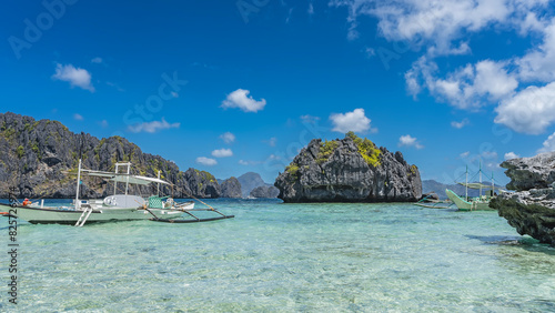 Traditional Filipino bangka boats are anchored in aquamarine bay. Picturesque steep karst cliffs rise above the ocean. Crystal clear water. Clouds in the blue sky. Philippines. Palawan. Big Lagoon. photo