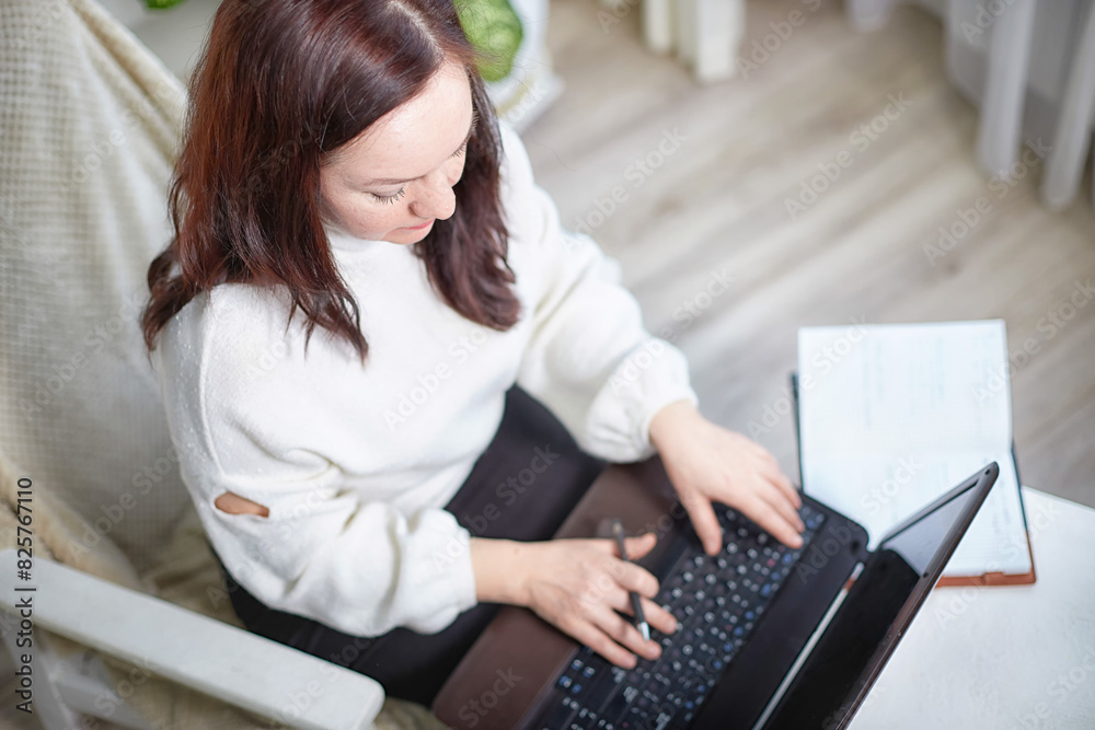 Fototapeta premium Middle aged Woman Working on Laptop at Home During Daytime. Mature female blogger, designer, writer, businesswoman in a cozy room alone