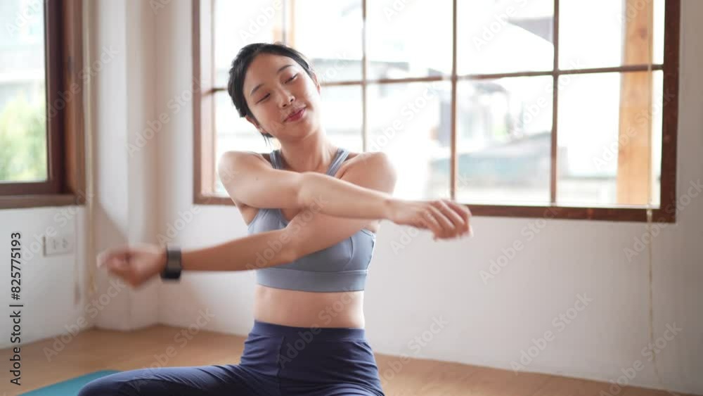 An Asian woman in a sports bra is stretching her arms at home. An Asian woman in a sports bra is stretching her arms at home.