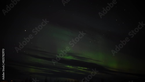 Night sky adorned with faint green Northern Lights, scattered stars, and dark clouds creating a mysterious and serene celestial scene