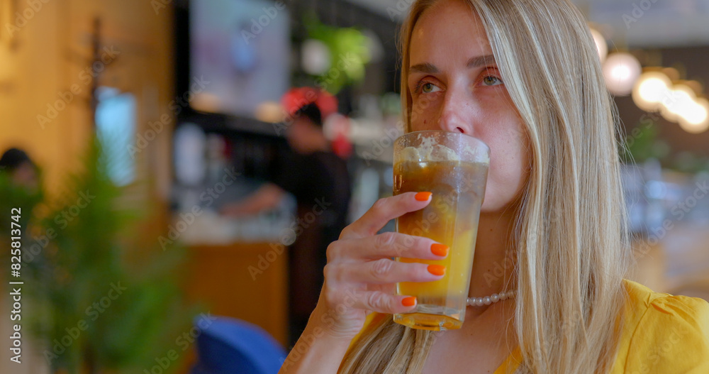 A blonde girl drinks iced coffee with orange juice in a cozy cafe A blonde girl drinks iced coffee with orange juice in a cozy cafe