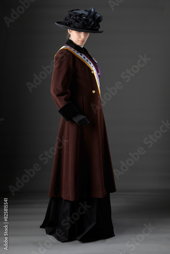 United Kingdom Victorian or Edwardian Suffragette wearing historically accurate purple and green sash and rosette against a plain studio backdrop