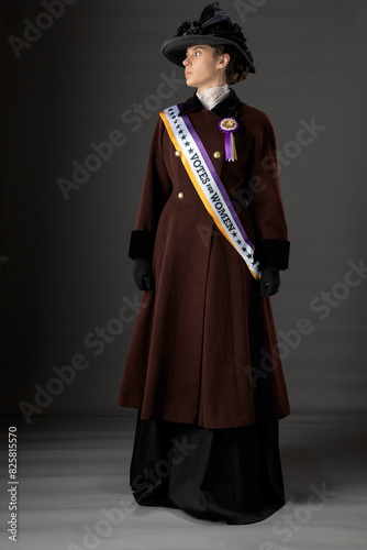 American Victorian or Edwardian Suffragette with historically accurate purple and gold sash and and rosette against a plain studio backdrop