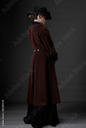 A Victorian or Edwardian woman wearing a winter coat and hat against a studio backdrop