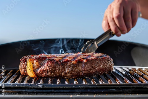 Capture a frontal view of a person grilling a succulent steak, showcasing the golden sear marks under a clear blue sky photo