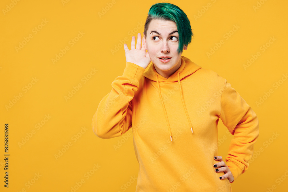 Young curious nosy happy woman with dyed green hair wear hoody casual clothes try to hear you overhear listening intently isolated on plain yellow orange background studio portrait. Lifestyle concept. Young curious nosy happy woman with dyed green hair wear hoody casual clothes try to hear you overhear listening intently isolated on plain yellow orange background studio portrait. Lifestyle concept.