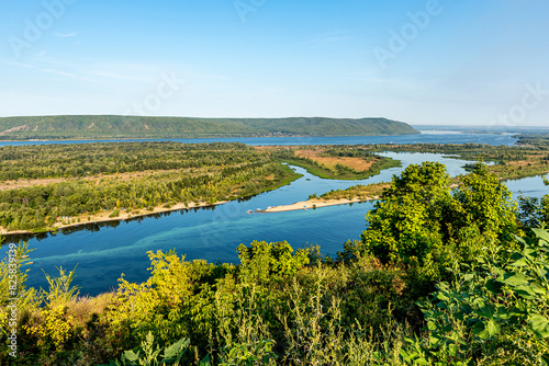 Zhiguli Mountains, Volga River and quiet backwater near the city of Samara, Russia. Blue water, sandy shore, tree, bush, ship. Quiet summer morning with light sky.
