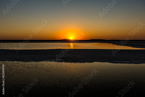 Sunset or sunrise on salt lake Baskunchak (Russia). Bright sun in a cloudless sky, calm brine in the saline. Morning or evening in summer, autumn or spring. photo