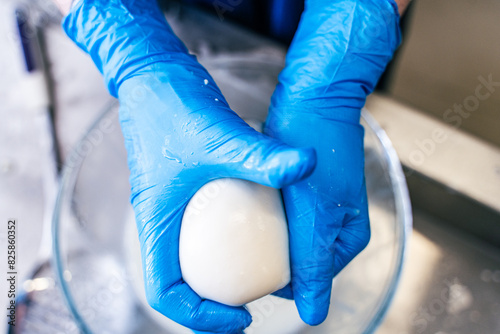 Close-up of mozzarella cheese rolling with blue-gloved hands. The process of making Italian cheese. photo