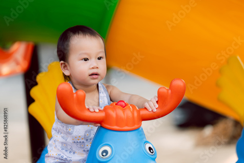Portrait of little boy playing with colorful spring rocking horse in the playground. In a moment of bright happiness, Child has saliva dripping down his chin. Baby son smiles sweetly. © Kanthita