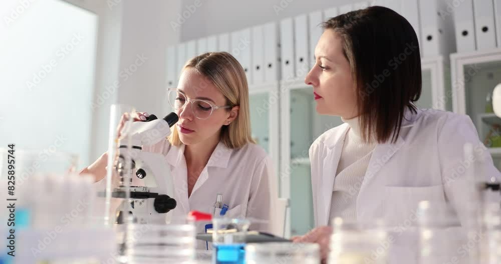 Scientist laboratory assistant looks through microscope and shows thumbs up to colleague Scientist laboratory assistant looks through microscope and shows thumbs up to colleague