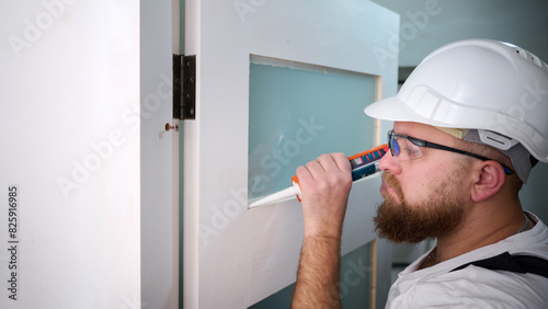 Construction worker using silicone sealant caulk. Accessories for assembling, install furniture, repair home. Man dressed in work attire, helmet and protective glasses. Caulk Sealant Application