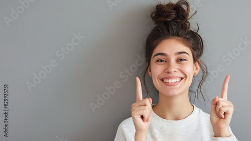 A cheerful young woman gestures upwards with her fingers against a neutral background