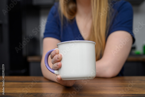 Kobieta siedzi w kuchni i trzyma w dłoni duży kubek z herbatą