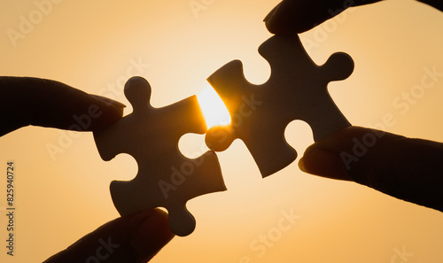 Silhouette of close up hand connecting a piece of jigsaw puzzle over sunlight effect. symbol of association,success and connection concept. business strategy.