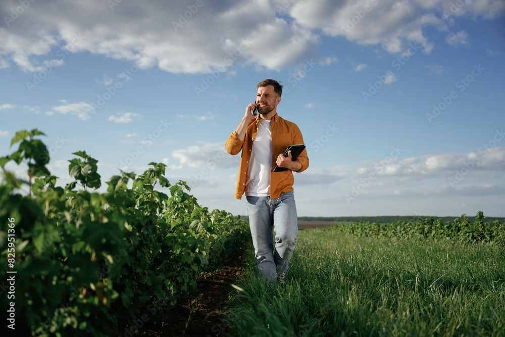 Talking by phone, holding notepad. Handsome man is on the agricultural field at daytime Talking by phone, holding notepad. Handsome man is on the agricultural field at daytime