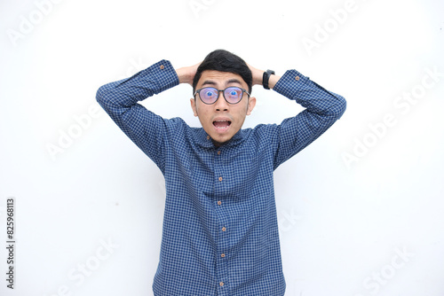 shocked expression with both hands on head, asian face in blue shirt and white isolated background.