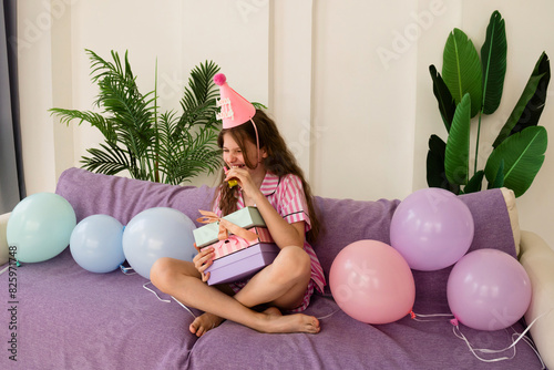 Girl laughing with party hat and holding birthday gifts. (ID: 825971748)