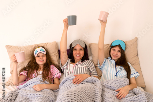 Happy family moment with mugs raised high in bed. (ID: 825972313)