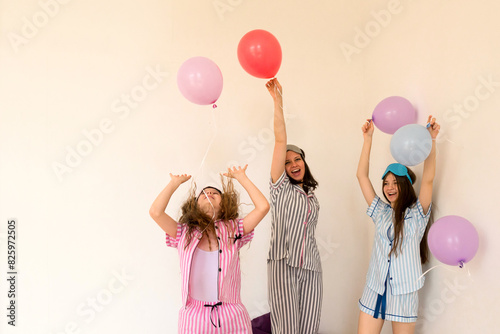 Woman and girls celebrating with balloons in pajamas at home. (ID: 825972505)