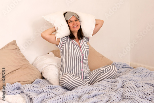 Woman smiling, holding pillows, sitting in cozy bed. (ID: 825972735)