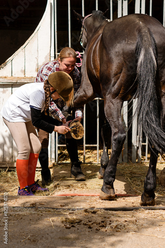 Girl receives guidance from instructor while cleaning horse's hoof.