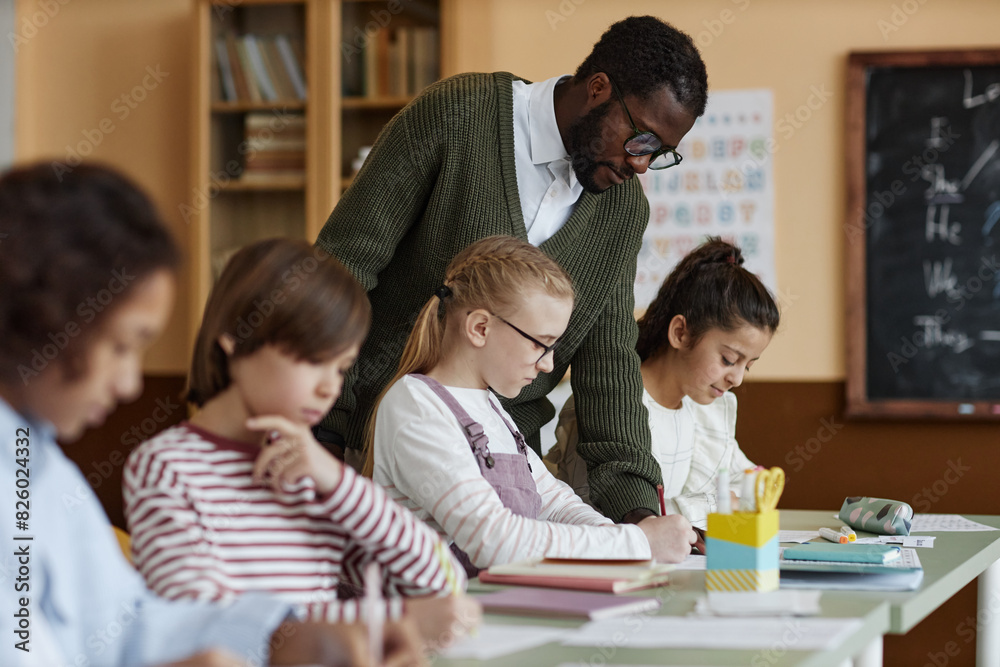 African American male teacher of English working in class watching kids doing writing exercise African American male teacher of English working in class watching kids doing writing exercise