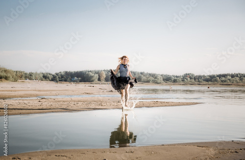 Portrait of beautiful 30 woman in dress running by the beach waving a long black skirt. Nature background. Copy space. Fashion concept. Energy of water and sun. Witch in state of pleasure and bliss