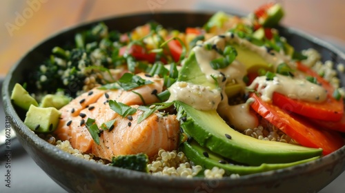 A healthy and colorful Buddha bowl filled with quinoa, roasted vegetables, avocado slices, and flaked salmon, drizzled with tahini dressing.