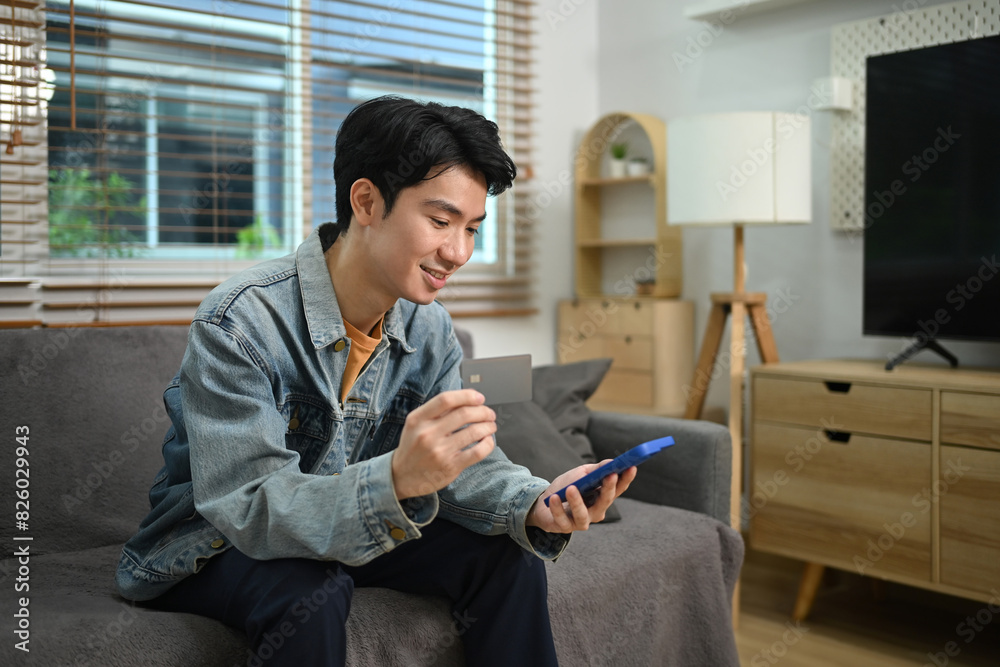 Handsome young man holding credit card using internet banking application on his smartphone Handsome young man holding credit card using internet banking application on his smartphone
