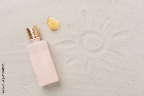 Sunscreen lotion with summer decor on sand background, top view