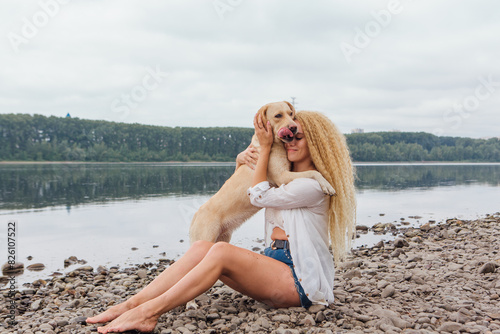 Young woman sitting with her labrador retriever dog on the river shore