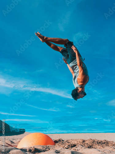 Man Performing Backflip at Beachfront With Urban Skyline Midday