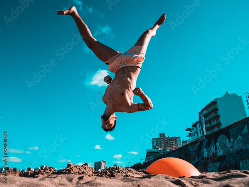 Man Performing flip at Beachfront With Urban Skyline Midday