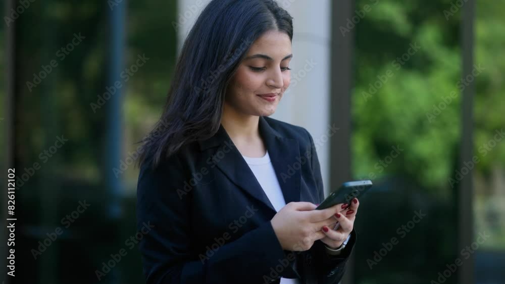 Successful young indian businesswoman hold smartphone scrolling social media texting browsing online checking email during break at work and looking ahead in modern business centre