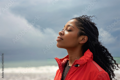 A woman stands on a sandy beach, gazing up at the sky above her