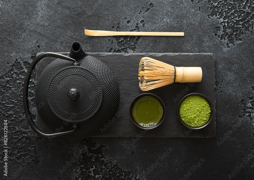 Organic matcha green tea powder with bamboo whisk and spoon and japanese traditional iron cast kettle on black background. Organic matcha green tea powder with bamboo whisk and spoon and japanese traditional iron cast kettle on black background.