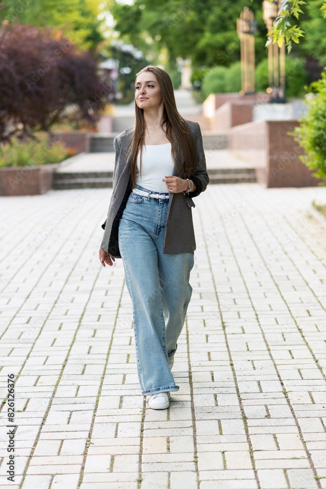 Fototapeta premium Pretty and attractive Caucasian young woman in stylish casual clothes posing with pleasure while walking in the park on a warm spring day. The concept of freedom, relax, style.