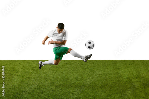 Dynamic photo of young athlete man, soccer player training to kicking ball in motion on green field against white studio background. Concept of professionals sport, competition, tournament, action. Ad